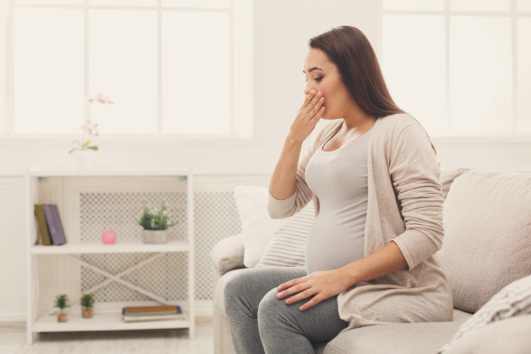 Young vomiting woman sitting on sofa
